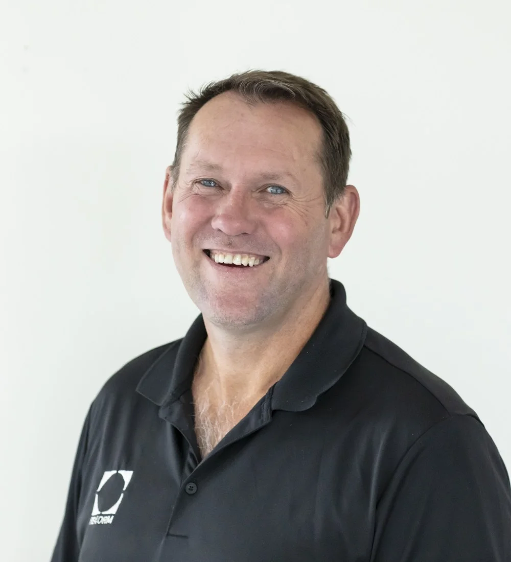 RE4ORM synthetic turf recycling &ndash; A man with short brown hair smiles at the camera, wearing a black collared shirt with a white logo on the left side, standing against a plain white background.
